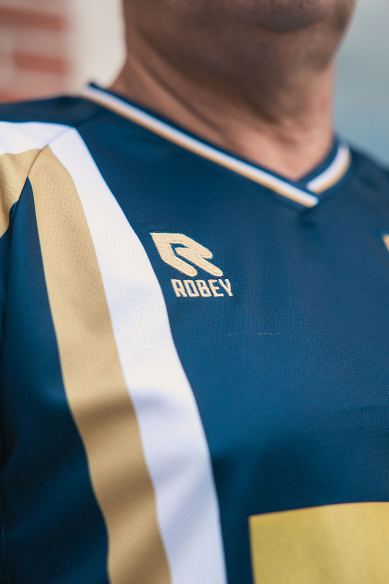 De gouden en witte baan over de borst van het derde shirt